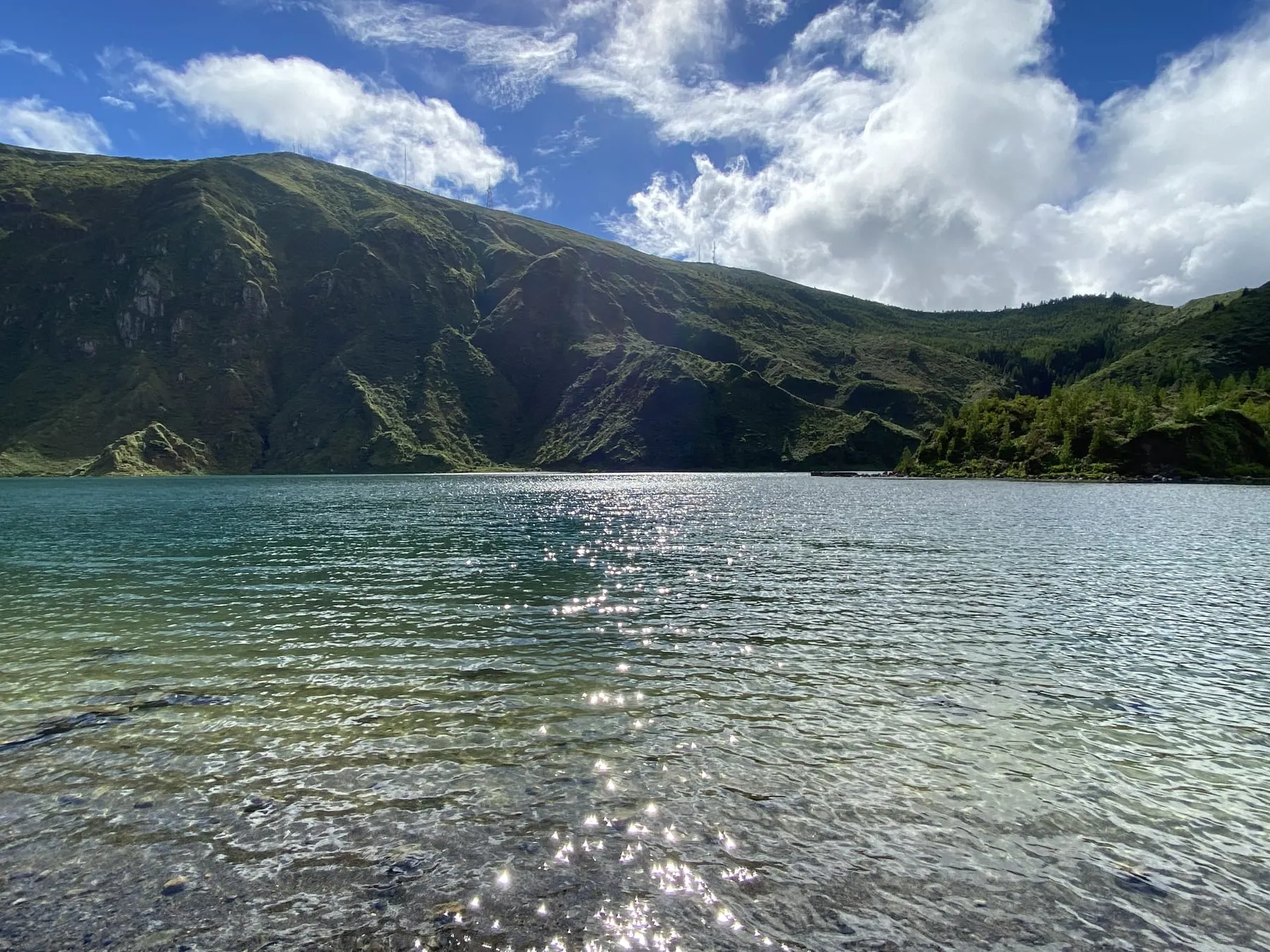 Sunlit lake water sparkling below a green mountainside