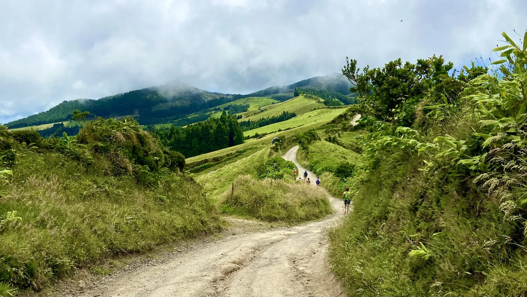 A dirt path winding over green hills towards a cloud-covered ridge